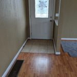 A narrow hallway with wooden and tiled flooring leading to a door with a window.
