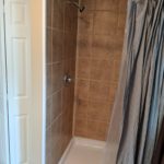 A small shower area with brown tiled walls and a gray shower curtain.