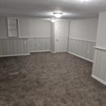 Empty carpeted room with white paneled walls and ceiling light.