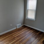 Empty room with wooden floor, grey walls, and a window with blinds.