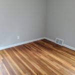 Empty room corner with hardwood flooring and white baseboards.