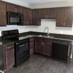 Modern kitchen with dark wood cabinets and black appliances.